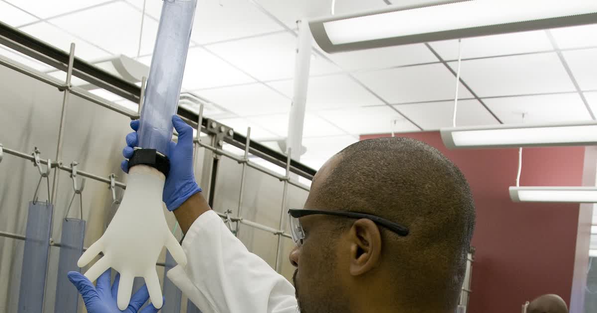 Worker in blue gloves testing a white medical glove on a tube