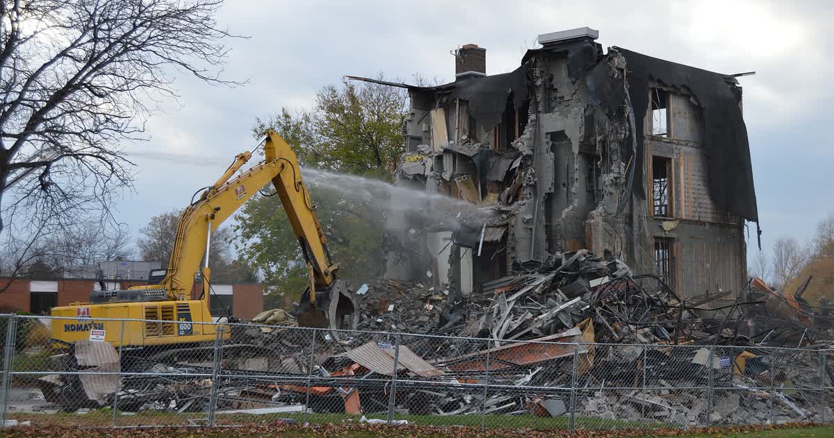 An excavator demolishing a commercial building while water sprays control dust