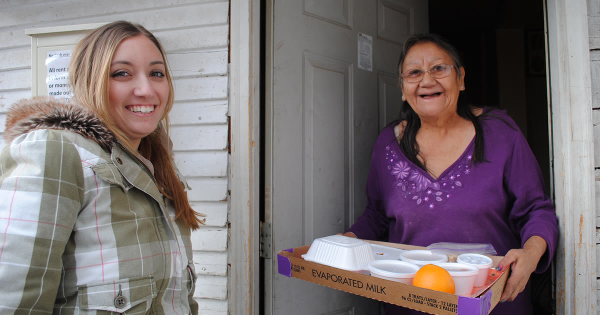 A volunteer delivering a meal to a senior at her front door