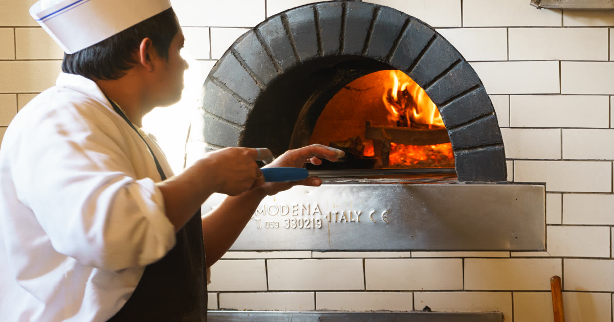 A chef at a wood-fired pizza oven