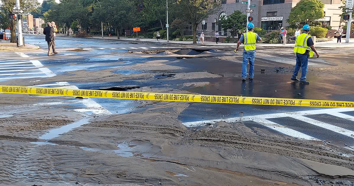 Workers survey a flooded street after a water main break