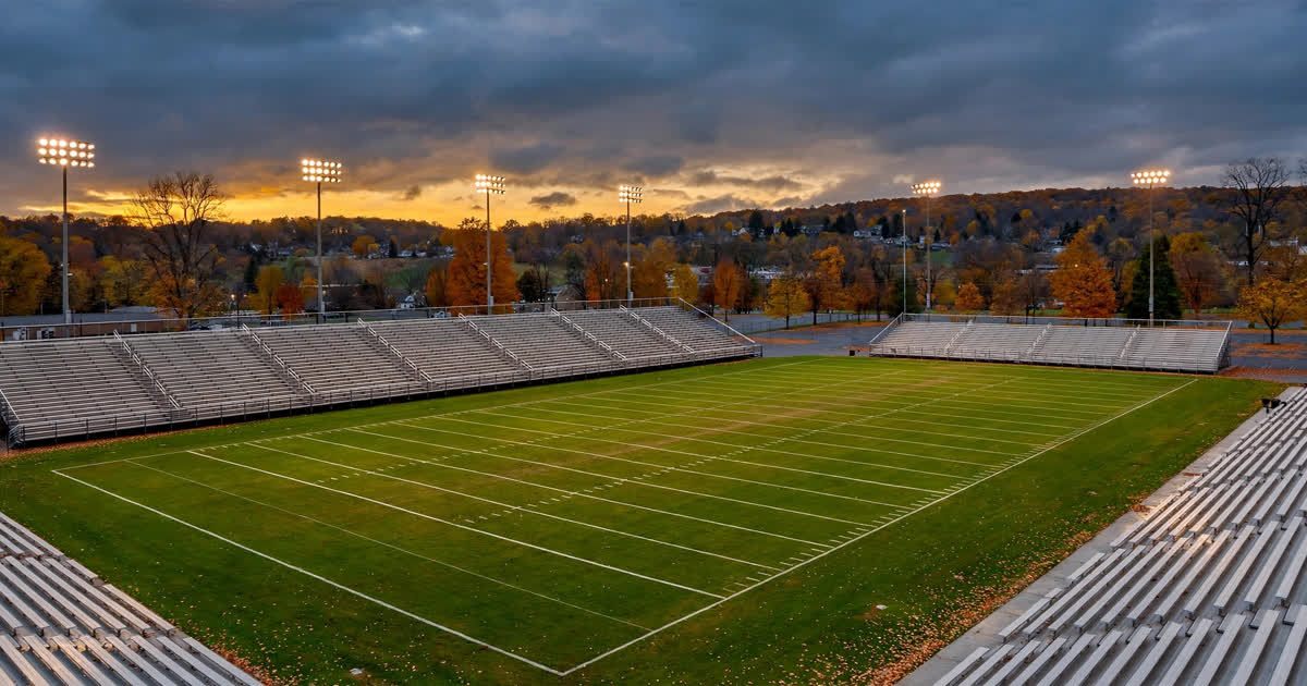 A high school football stadium at dusk under the lights in autumn