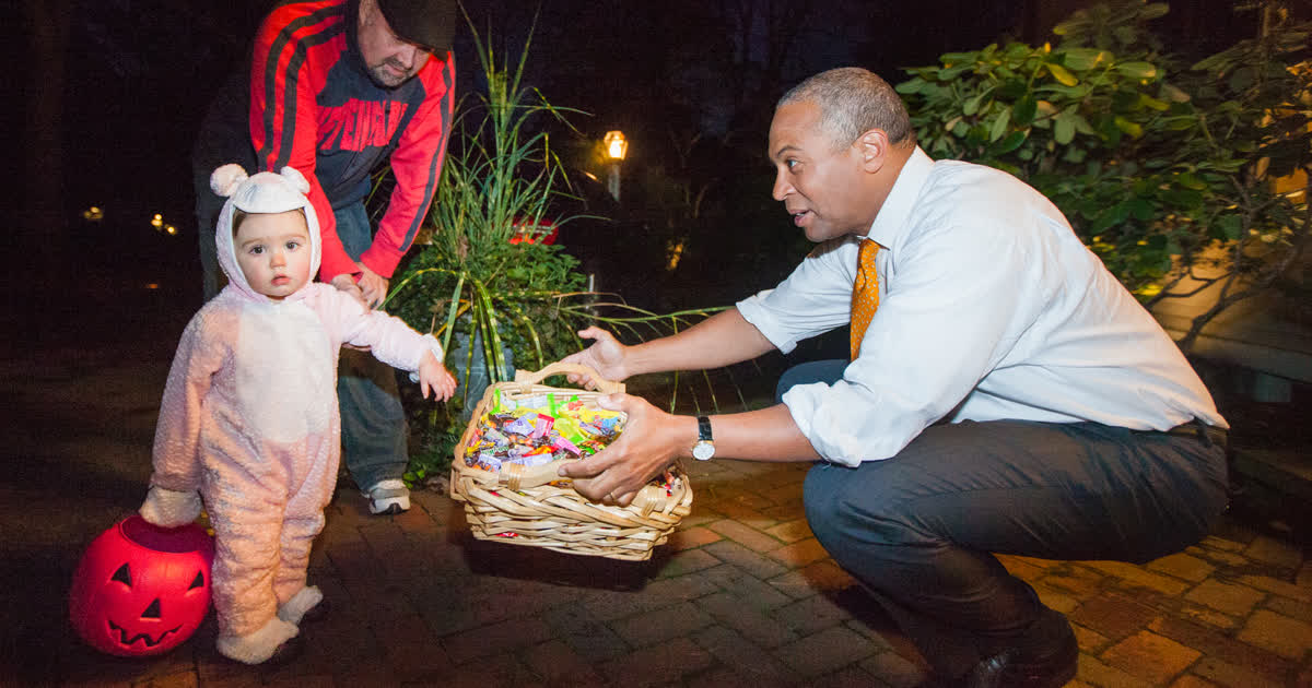 A young trick-or-treater in costume with a pumpkin bucket receiving candy