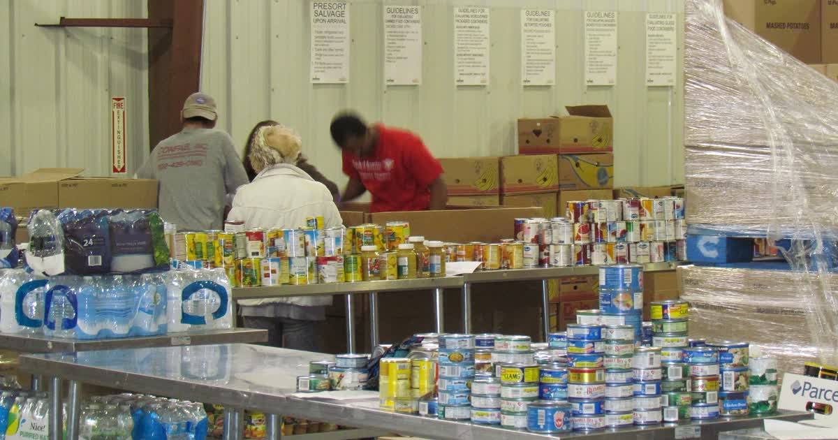 Volunteers sort canned food and bottled water donations on tables inside a food bank warehouse
