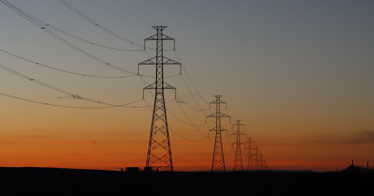 Electric transmission towers and power lines silhouetted at sunset
