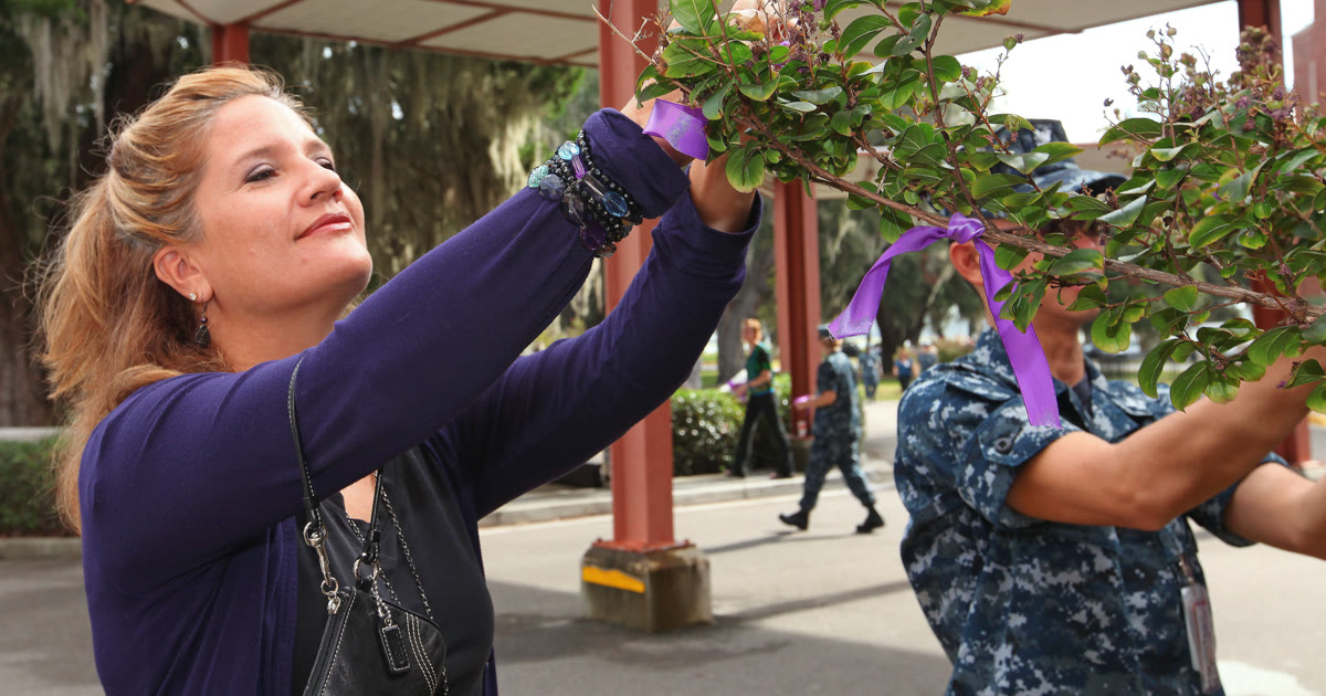 Woman tying a purple domestic violence awareness ribbon onto a tree branch