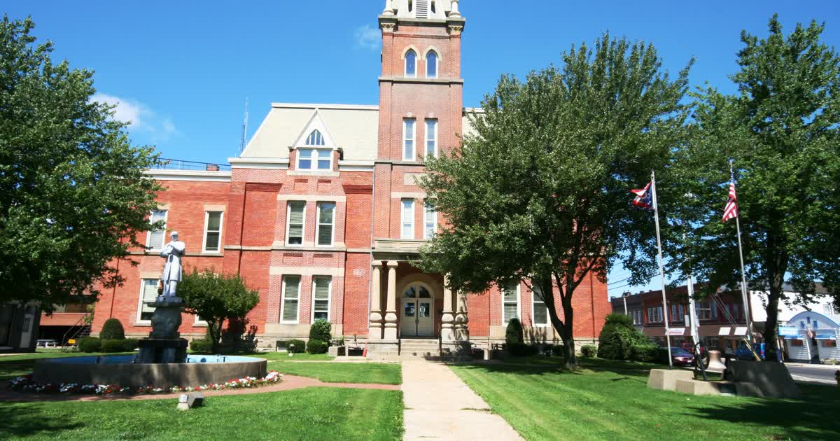 The Ashtabula County Courthouse in Jefferson, Ohio, a red-brick building with a tower, Ohio and U.S. flags, and a statue on the lawn