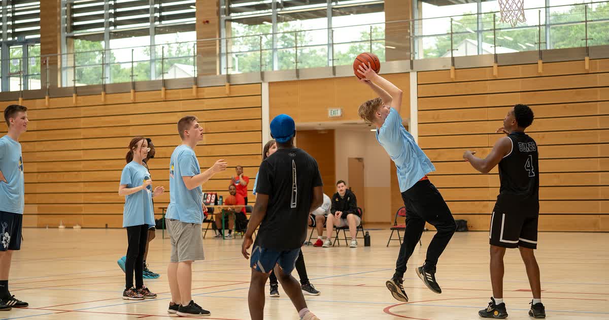 Young basketball players on an indoor court, one shooting the ball toward the hoop