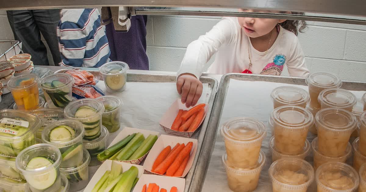 An elementary school student chooses vegetables in a school cafeteria line