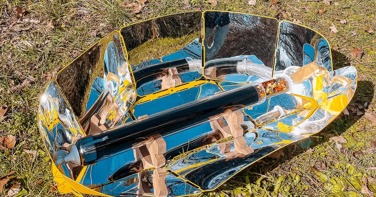 A solar cooker with a glass vacuum tube cooking food outdoors on grass