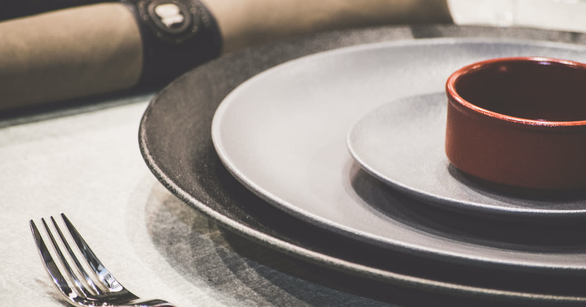 An empty ceramic bowl on a plate at a set table, ready to be filled