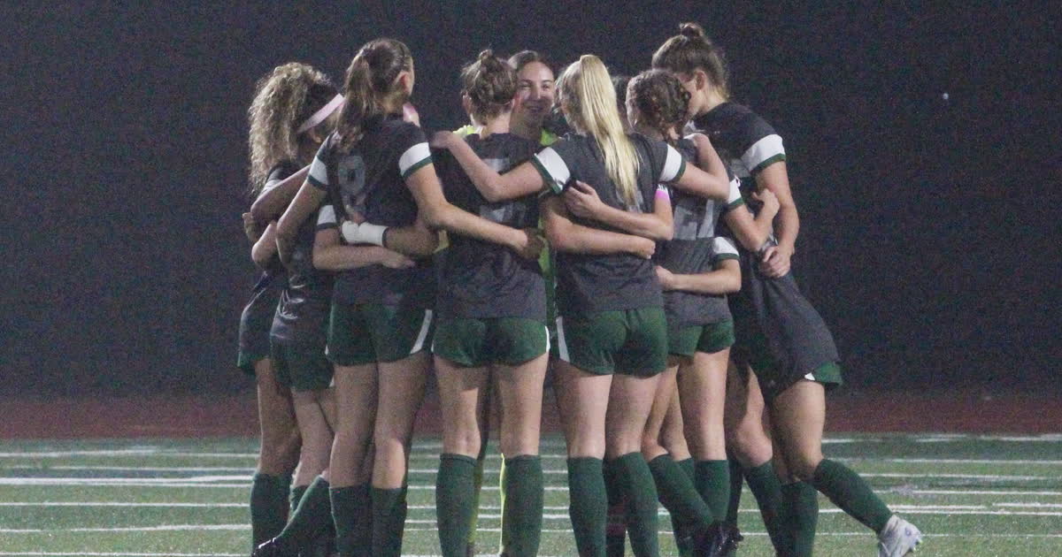 A girls high school soccer team huddles together on the field at night after a win