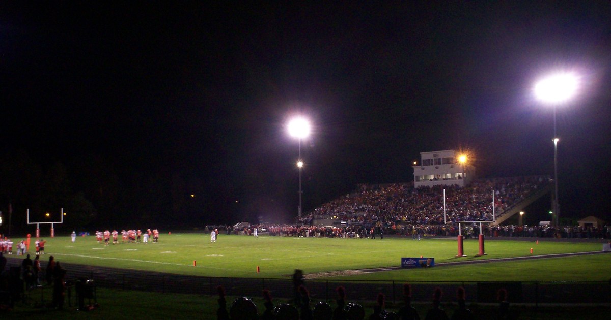 High school football stadium under the lights at night with a packed crowd